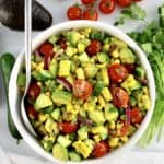 Corn Avocado Salad in white bowl with silver serving spoon and veggies in back