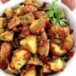 German Potato Salad in white bowl with chopped bacon and parsley on top