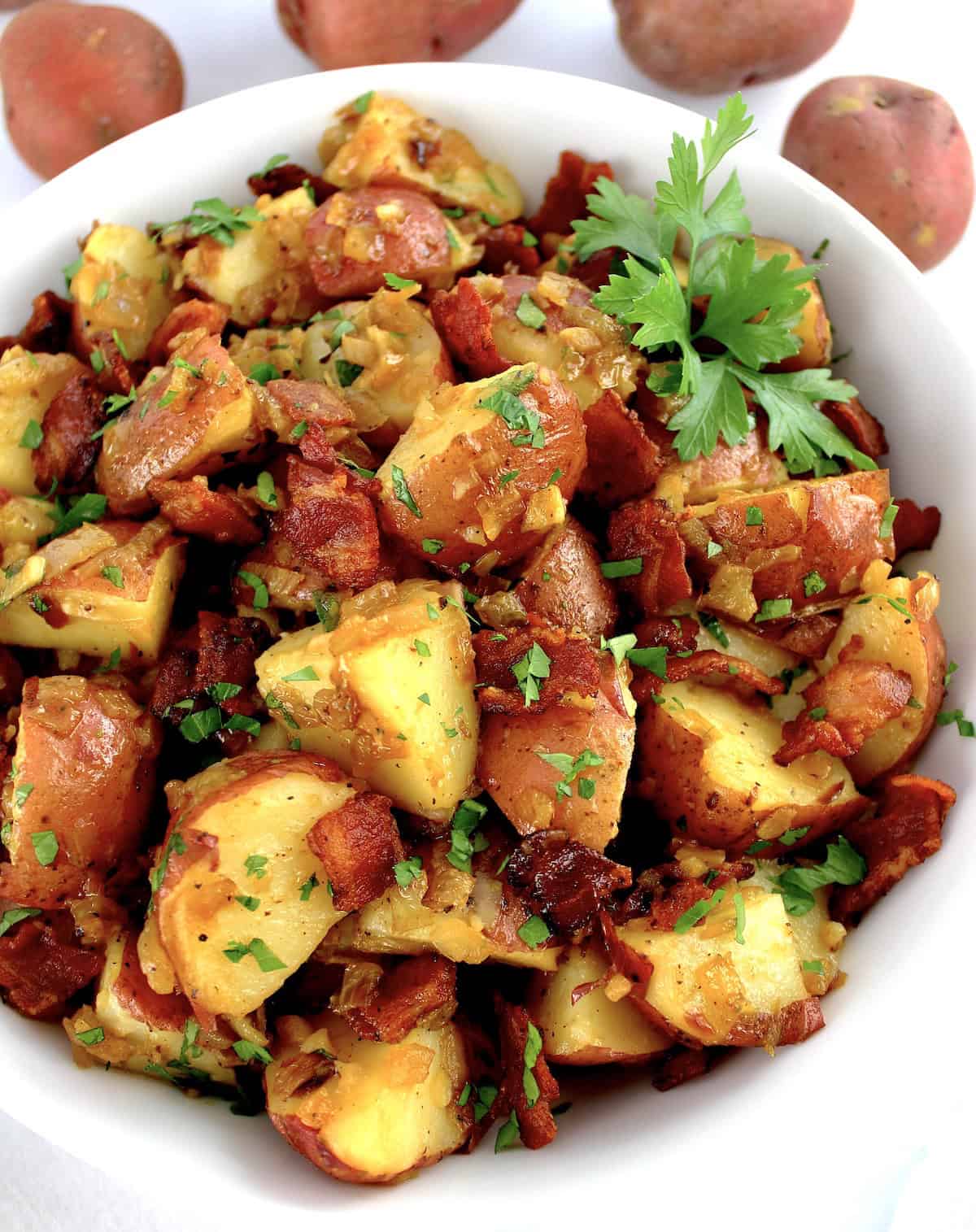 German Potato Salad in white bowl with chopped bacon and parsley on top