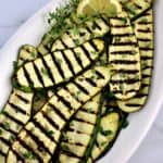 Grilled Zucchini slices on white oval platter with sprig of thyme and lemon slices