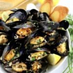 Drunken Mussels in white bowl with chopped parsley lemon wedges and 2 baguette slices