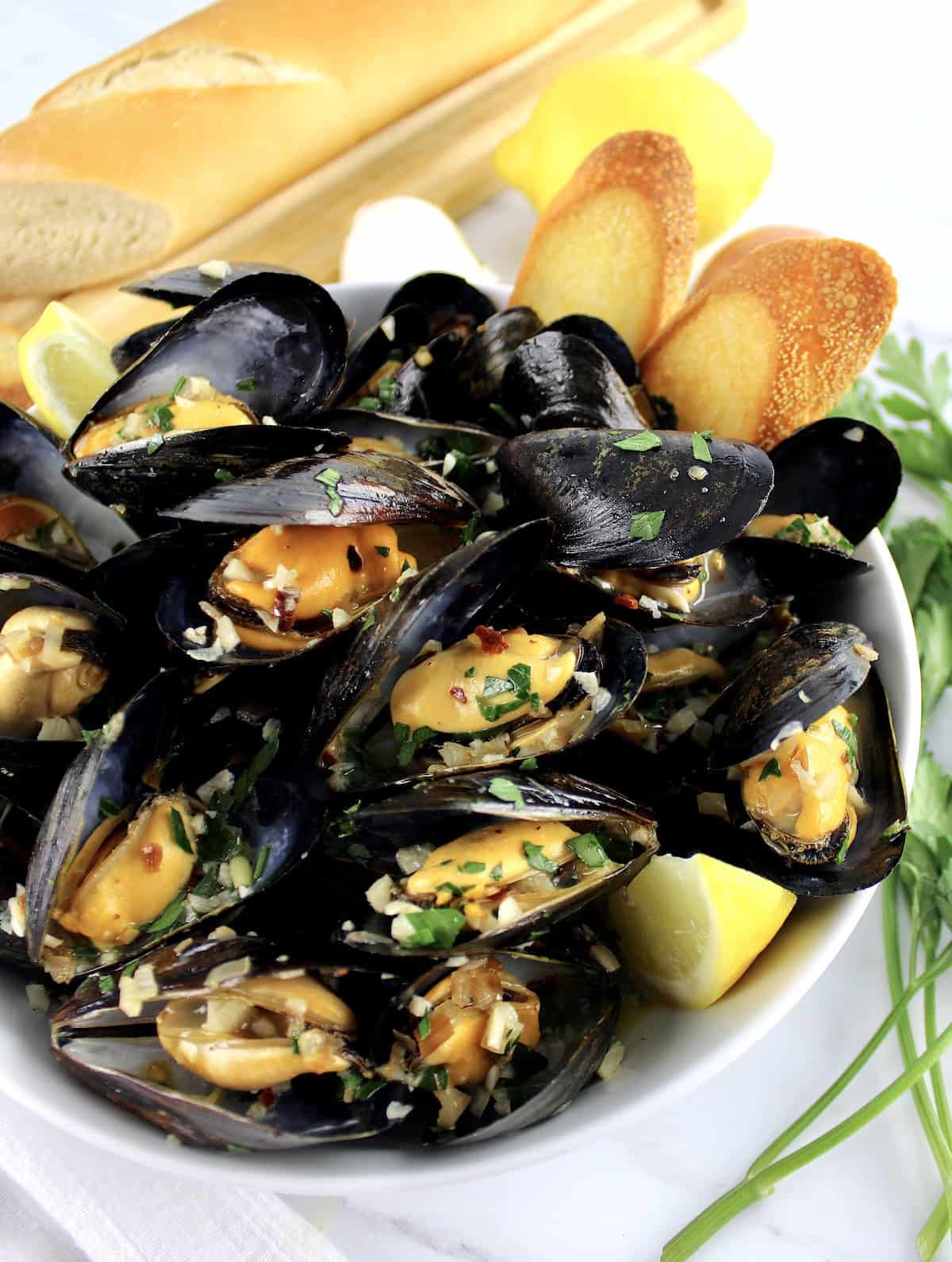 Drunken Mussels in white bowl with chopped parsley lemon wedges and 2 baguette slices