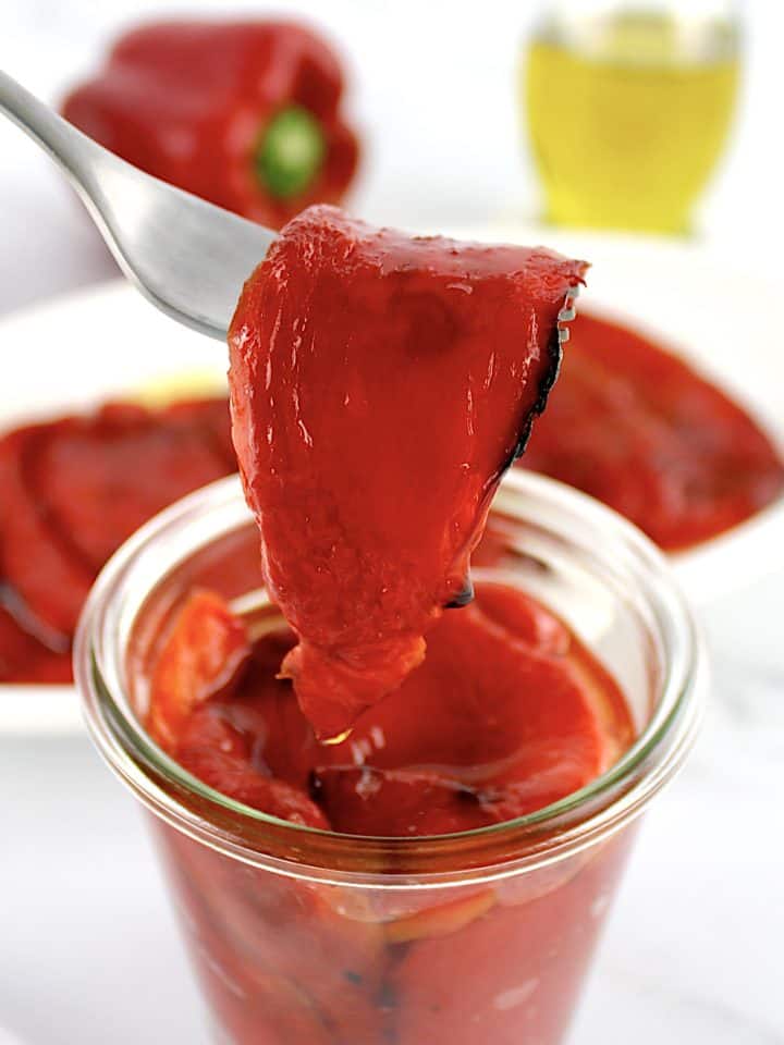 Roasted Red Peppers in open glass jar with one held up with fork
