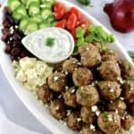 Greek Meatballs on white platter with cucumbers, tomatoes, olives and dip