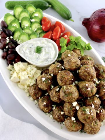 Greek Meatballs on white platter with cucumbers, tomatoes, olives and dip