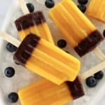 Mango Blueberry Popsicles on white oval platter with crushed ice and fresh blueberries around