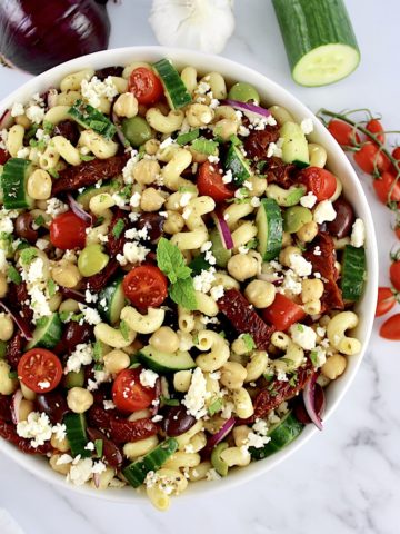 Mediterranean Pasta Salad in white bowl with veggies in back