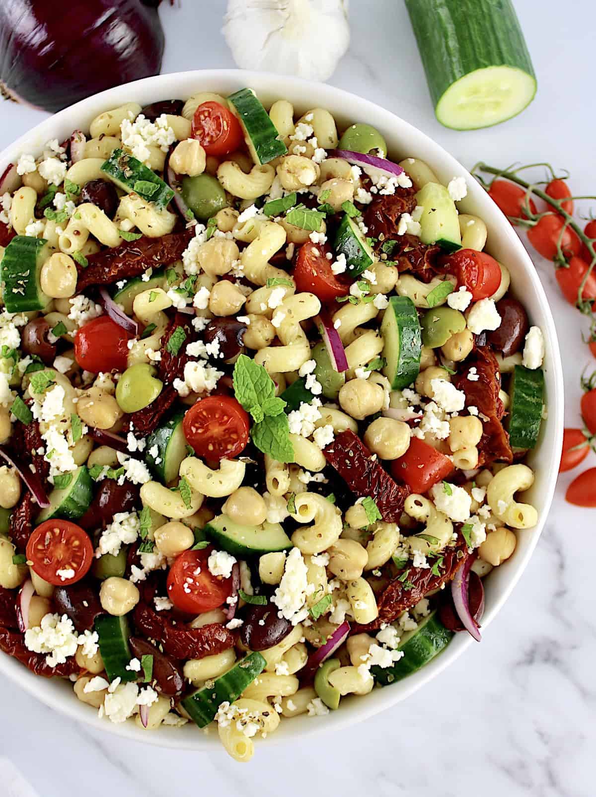 Mediterranean Pasta Salad in white bowl with veggies in back