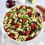 Mediterranean Pasta Salad in white bowl with veggies in back