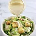 Caesar Salad Dressing being poured over salad with croutons