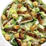 Chicken Caesar Salad in white bowl with strips of chicken and croutons