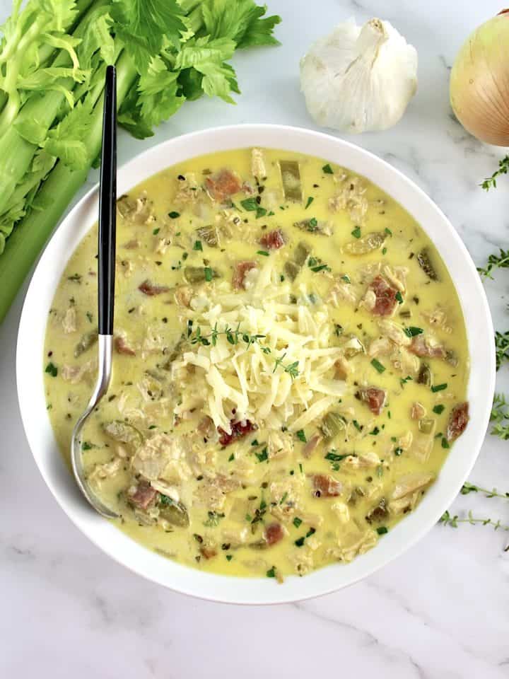 Chicken Cordon Bleu Soup in white bowl with spoon and celery, onion and garlic in back