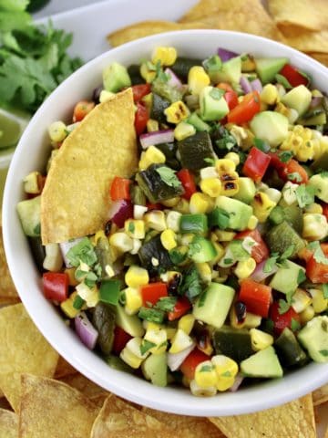 Roasted Corn and Poblano Salsa in white bowl with tortilla chip