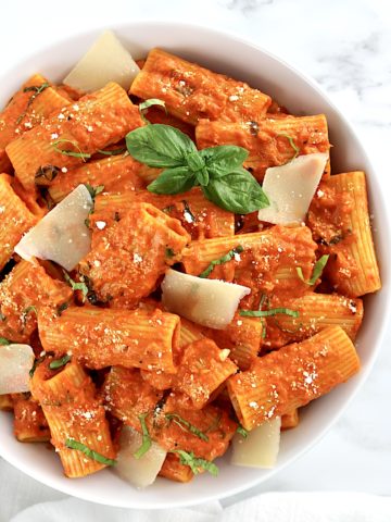 Roasted Pepper Pasta in white bowl with shaved parmesan and fresh basil on top