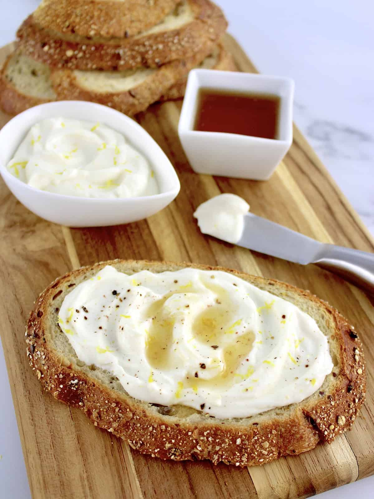 Whipped Ricotta Toast on cutting board with ricotta and honey in back