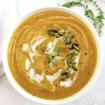 Butternut Squash Soup in white bowl with pumpkin seeds and drizzle of cream on top