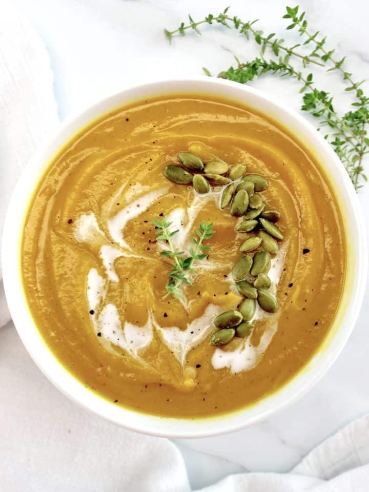 Butternut Squash Soup in white bowl with pumpkin seeds and drizzle of cream on top