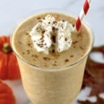 pumpkin milkshake in glass with whip cream and pumpkin pie spice on top with a red and white straw