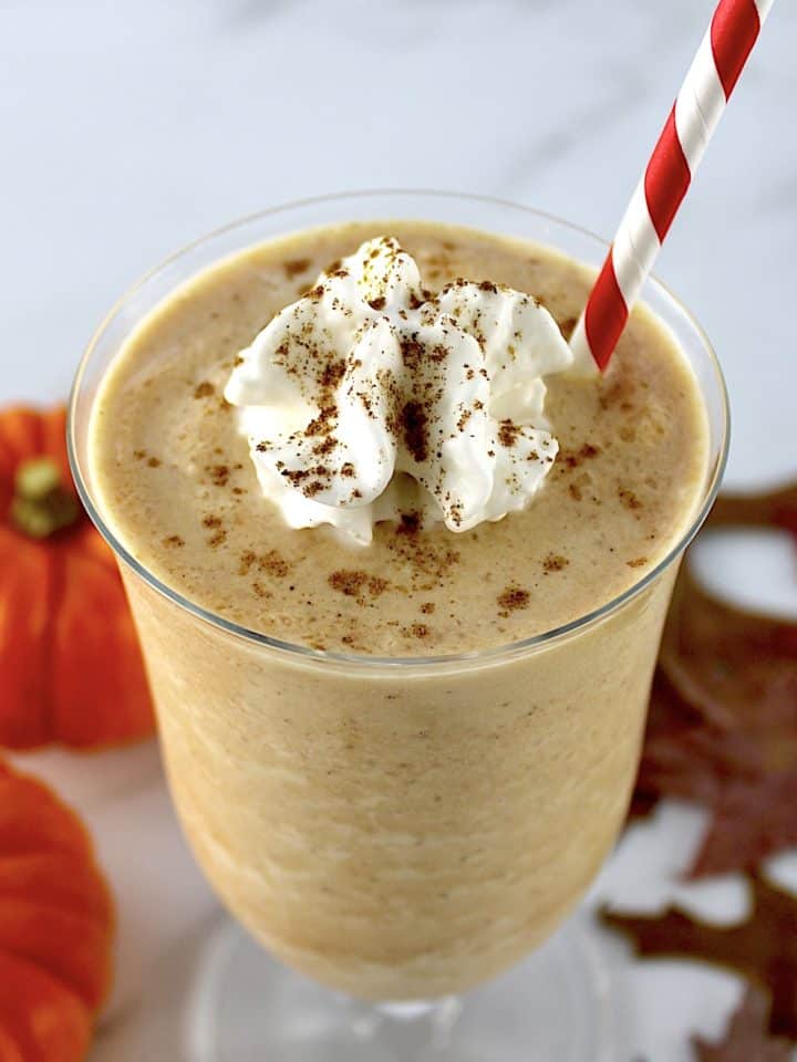 pumpkin milkshake in glass with whip cream and pumpkin pie spice on top with a red and white straw