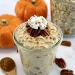 Pumpkin Pie Overnight Oats in open glass jar with whip cream on top and pumpkins in back