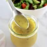 Maple Dijon Vinaigrette being spooned out of open glass jar with salad in back