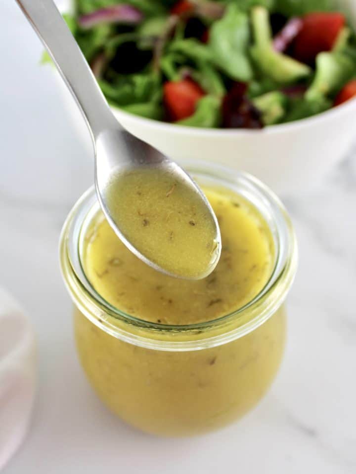 Maple Dijon Vinaigrette being spooned out of open glass jar with salad in back