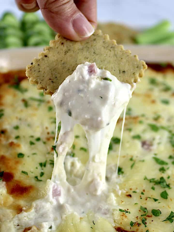 Chicken Cordon Bleu Dip being scooped out with cracker and cheese pulling