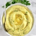 Italian Cheesy Mashed Potatoes in white bowl with pat of butter in center and serving spoon