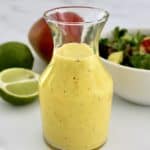 closeup of Mango Dressing in glass bottle with mango, lime and salad in back