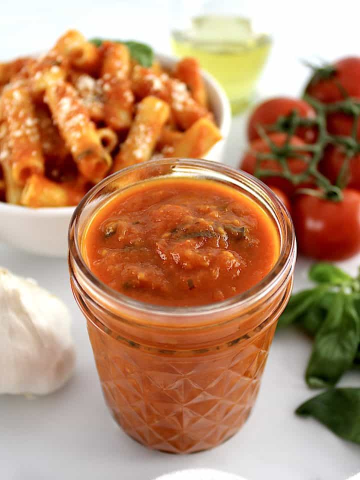 Roasted Tomato Sauce in open glass jar with pasta and tomatoes in back