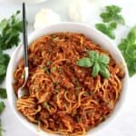 Spaghetti with Meat Sauce in white bowl with fork with spaghetti wrapped around and basil leaf on top