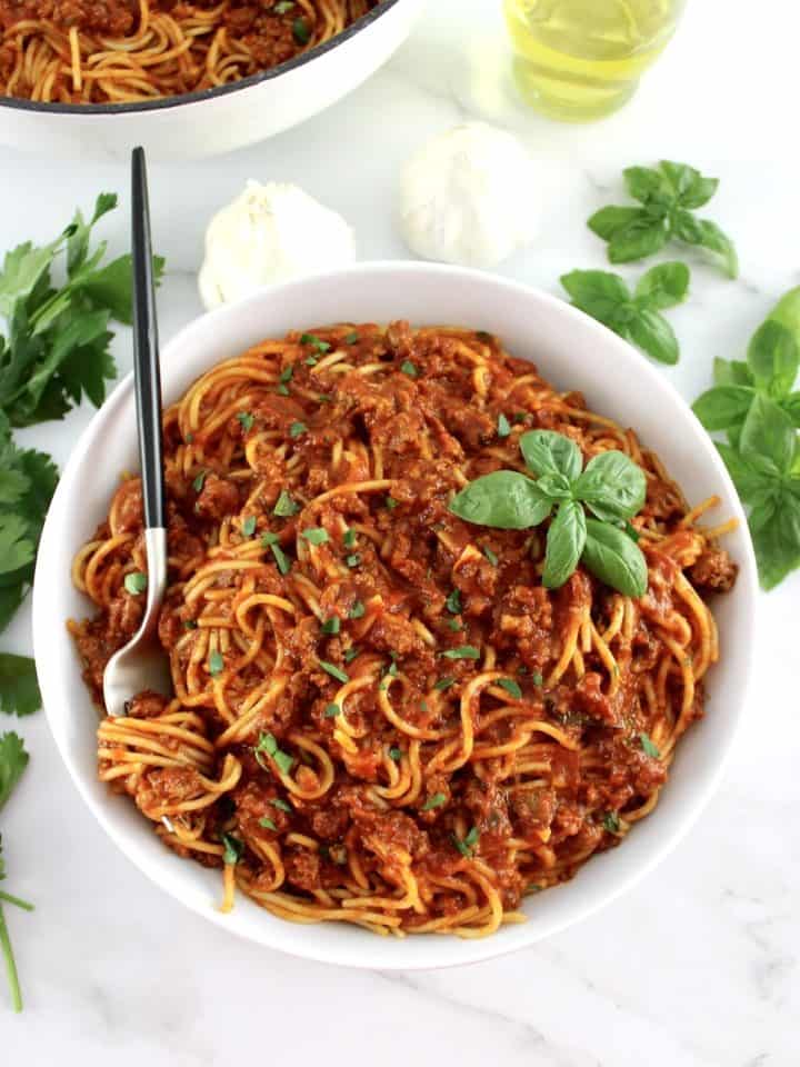 Spaghetti with Meat Sauce in white bowl with fork with spaghetti wrapped around and basil leaf on top