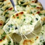 Spinach Artichoke Stuffed Shell being lifted out of casserole with cheese pull