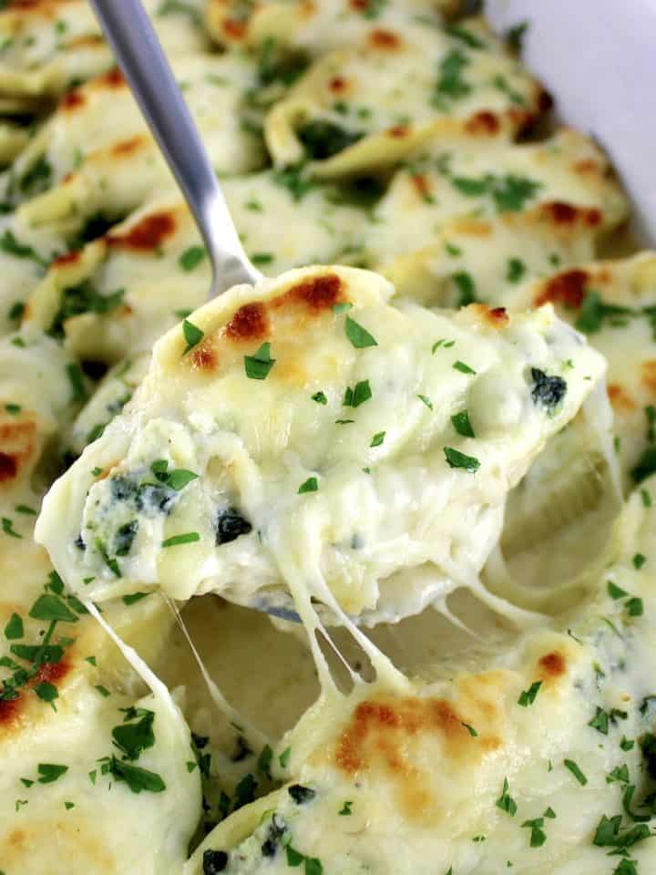 Spinach Artichoke Stuffed Shell being lifted out of casserole with cheese pull