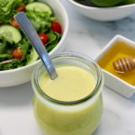 Honey Lime Vinaigrette in open glass jar with spoon in it, salad, honey and lime in back