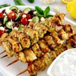 Air Fryer Greek Chicken Souvlaki on white platter with tzatzi sauce and Greek salad on side