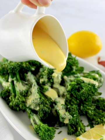 Beurre Blanc Sauce being poured out over broccoli on white plate with lemon in back