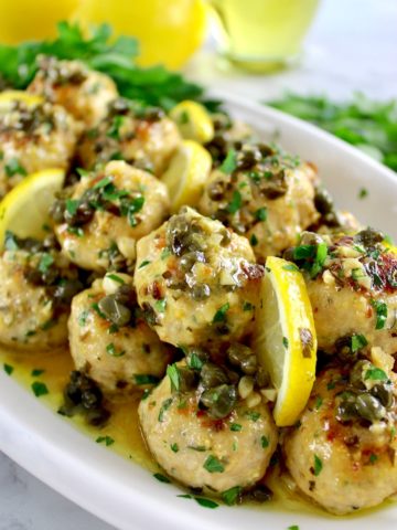 Chicken Piccata Meatballs on white platter with chopped parsley and lemon slices