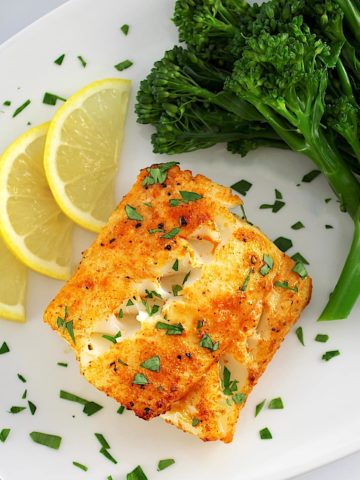 Easy Air Fryer Cod on white plate with broccoli and 3 lemon slices