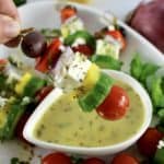 Greek Salad Skewer being held up over dressing in white cup