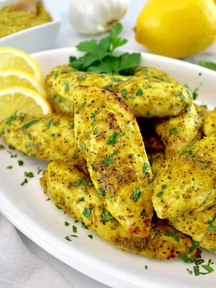 Air Fryer Lemon Pepper Chicken Tenders piled up on white oval plater with lemon slices and parsley