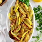 Greek Lemon Potatoes on white oval platter with lemon slices and parsley with serving spoon on side